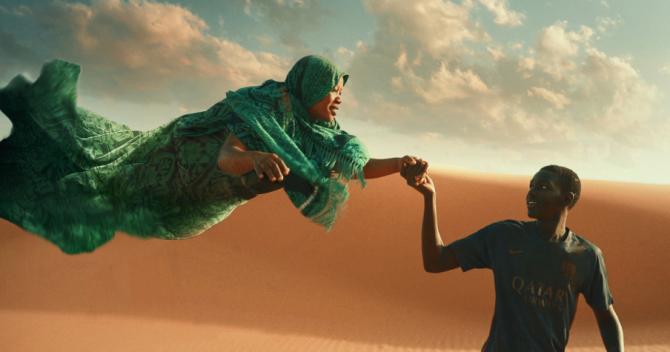 Chlapec a vznášející se žena se drží za ruce. Za nimi poušť.