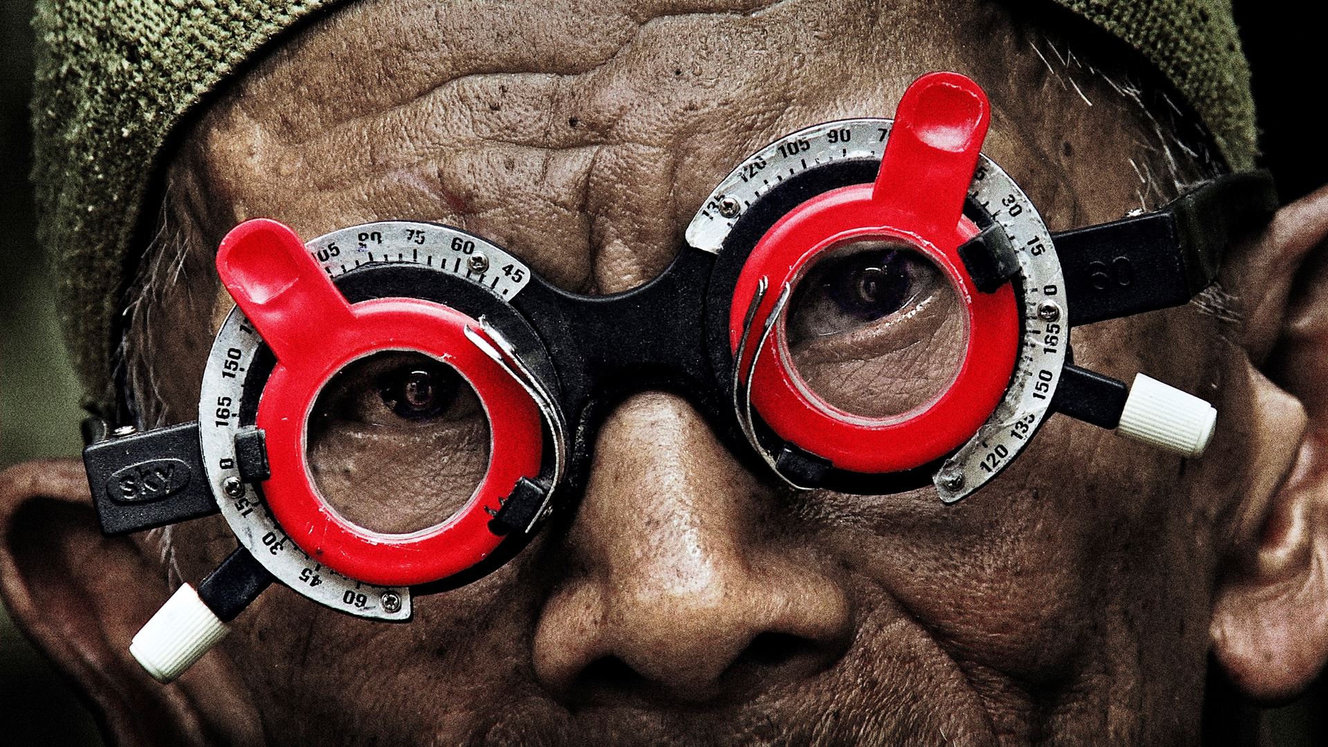 Starší muž z Indonésie má na sobě brýle, které mu měří dioptrie. Kouká do kamery. 