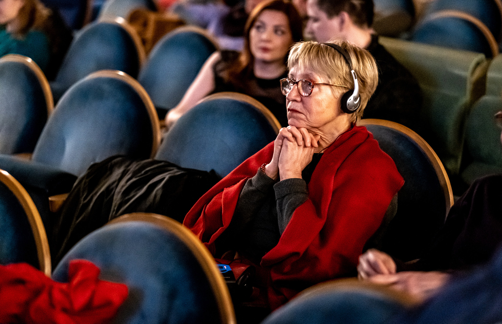 Přístupný festival / Festival Accessibility Divačka v hledišti kina se sluchátky s audiopopisem.