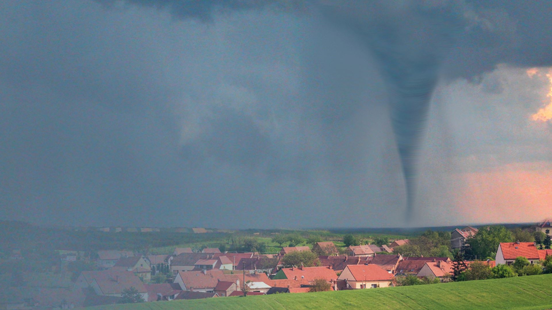 Tornádo – rok poté Fotografie krajiny s moravskou vesničkou v dešti. V pozadí se blíží tornádo.