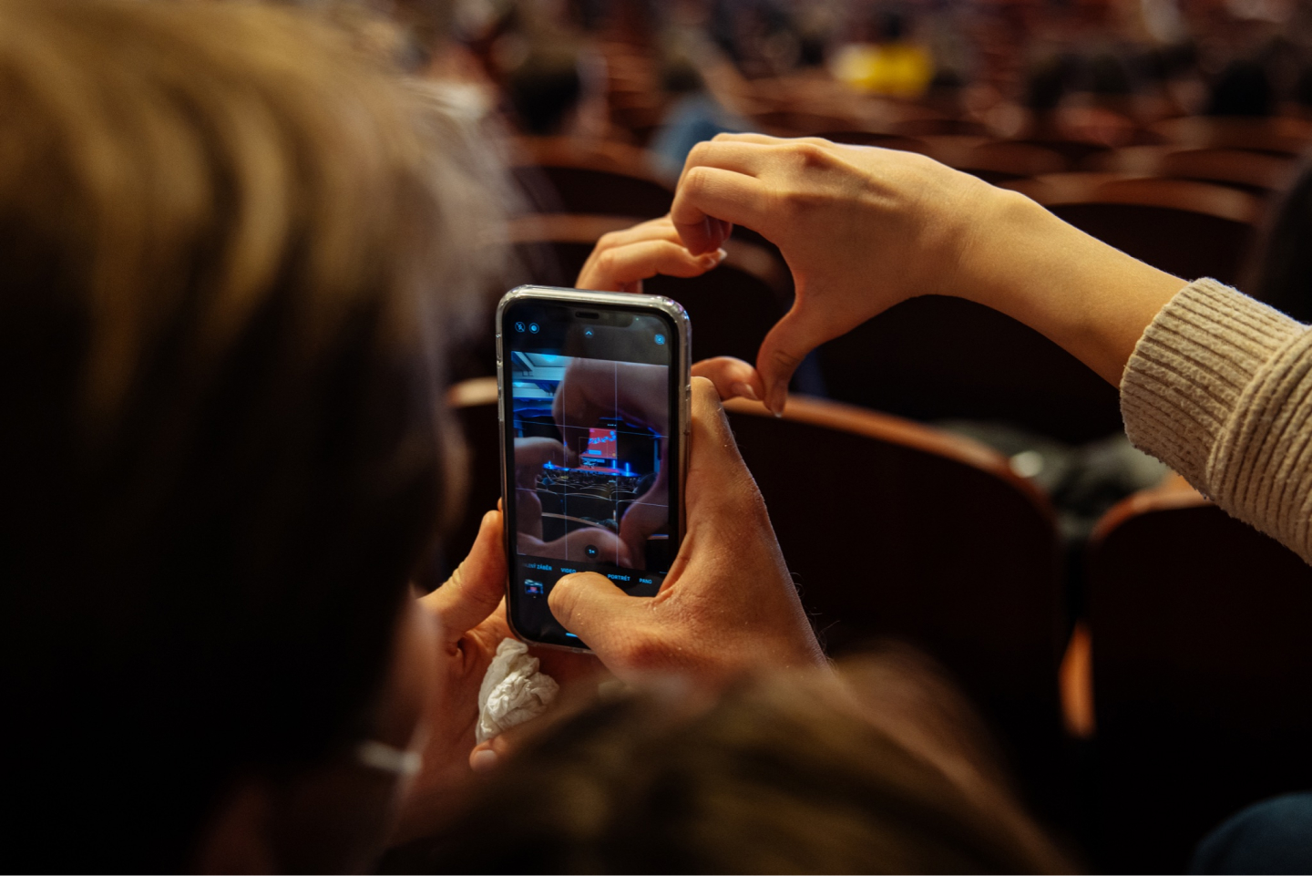 Divák v kině drží v ruce mobilní telefon a fotí si projekční plátno