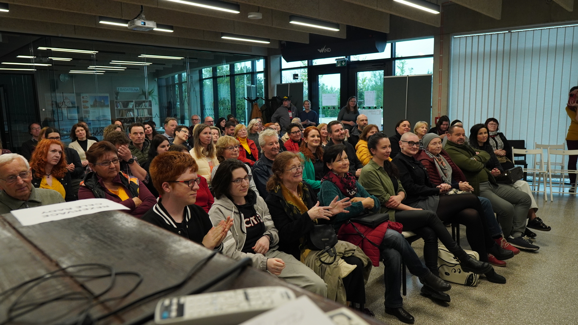 Přednáškový sál plný sedících lidí, kteří tleskají.