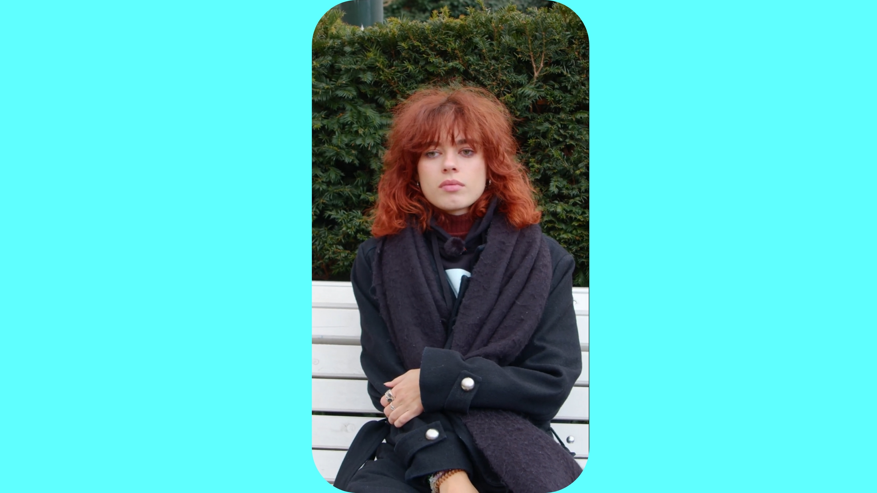 Žena v kabátě sedí na lavičce.