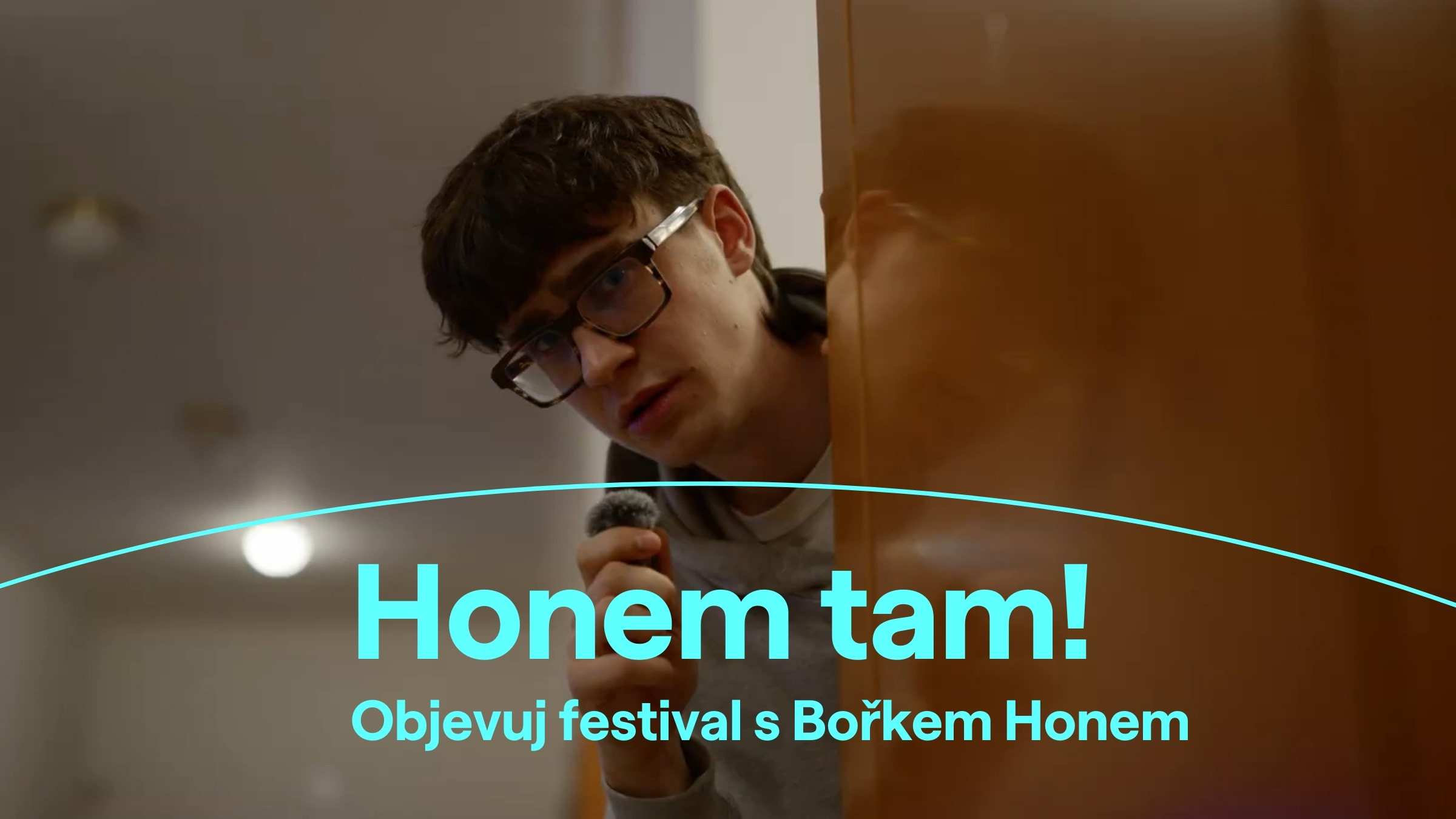 Mladý muž s brýlemi vykukuje zpoza dveří a drží v ruce malý mikrofon. Na fotce je vizuál festivalu s nápisem: Honem tam! Objevuj festival s Bořkem Honem.