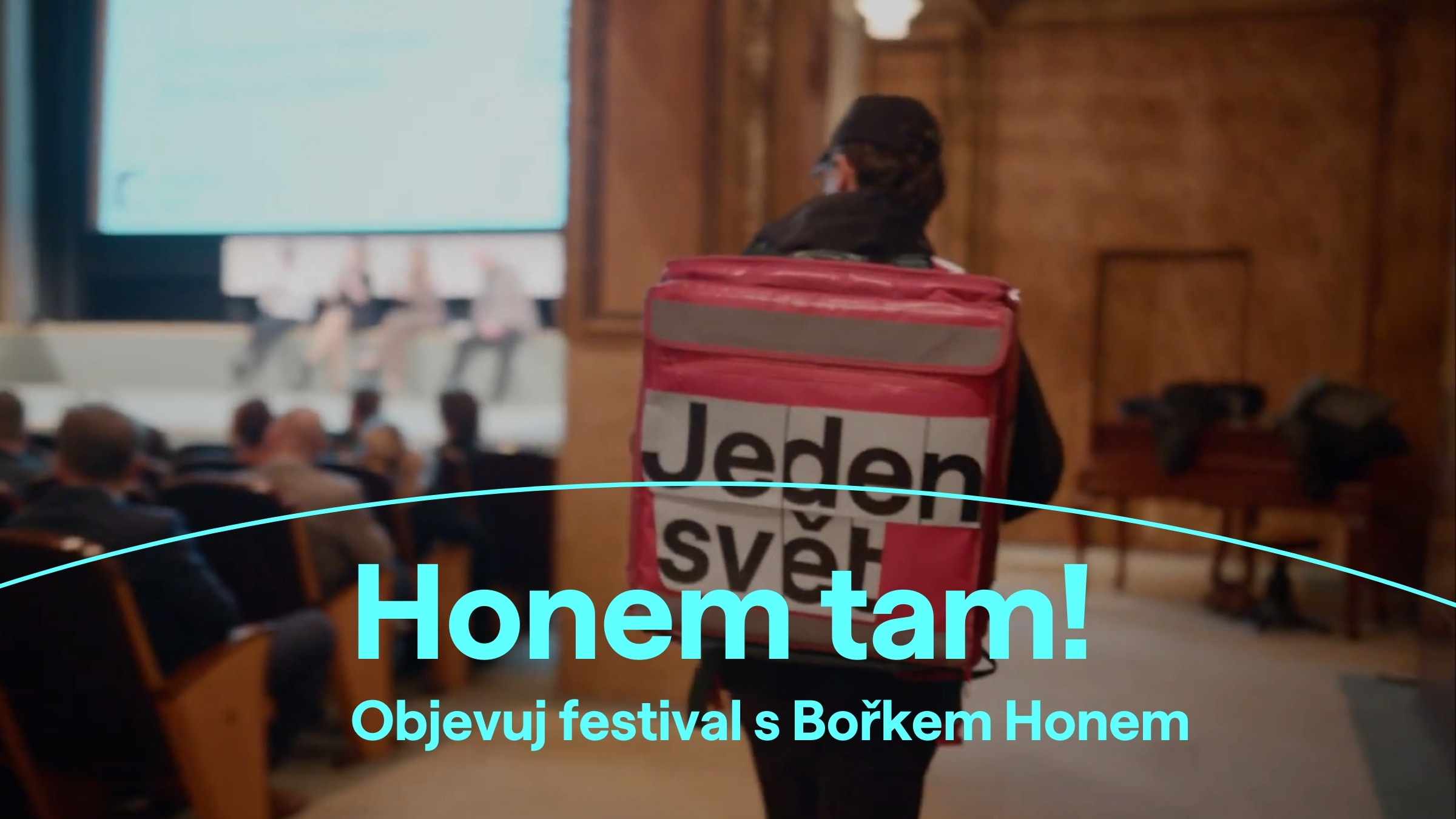 Muž kráčí po kinosálu s batohem kurýra, na kterém je nápis Jeden svět. Na fotce je vizuál festivalu s nápisem: Honem tam! Objevuj festival s Bořkem Honem.