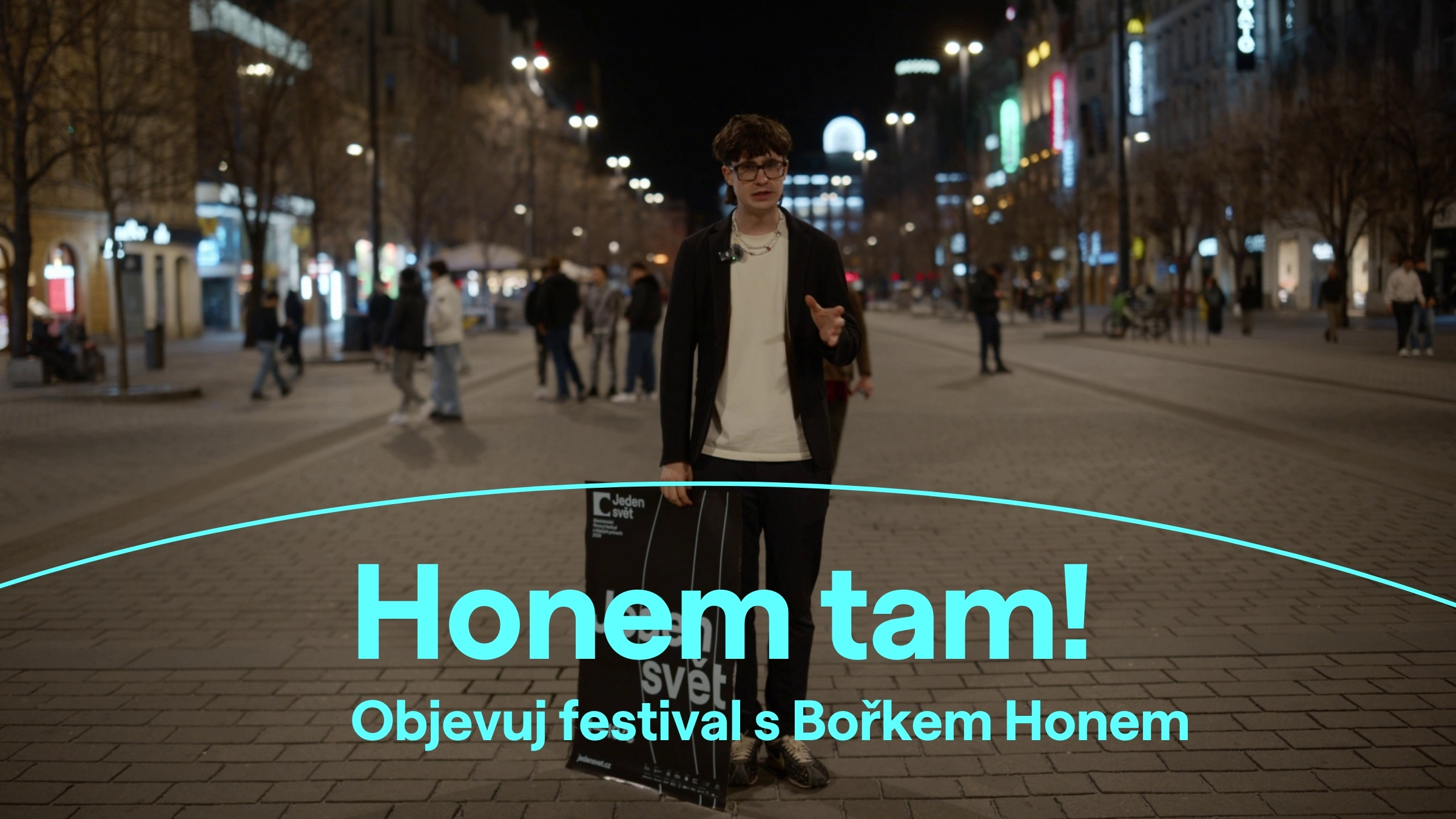 Muž stojí na ulici s plakátem Jednoho světa. Na fotce je vizuál festivalu s nápisem: Honem tam! Objevuj festival s Bořkem Honem.