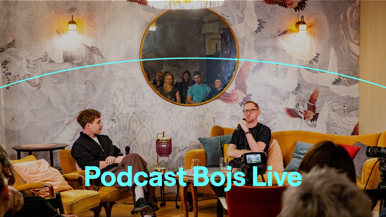 Grafika, na které je fotografie dvou mužů sedících na pohovce a v křesle, vedoucích spolu hovor. Dole je text: Podcast Bojs Live.