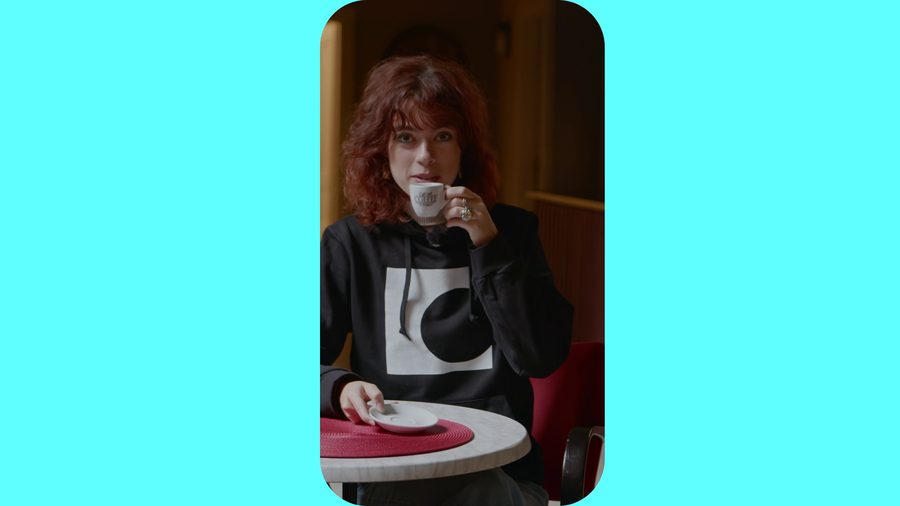 Žena sedí u stolu a drží v ruce šálek kávy.