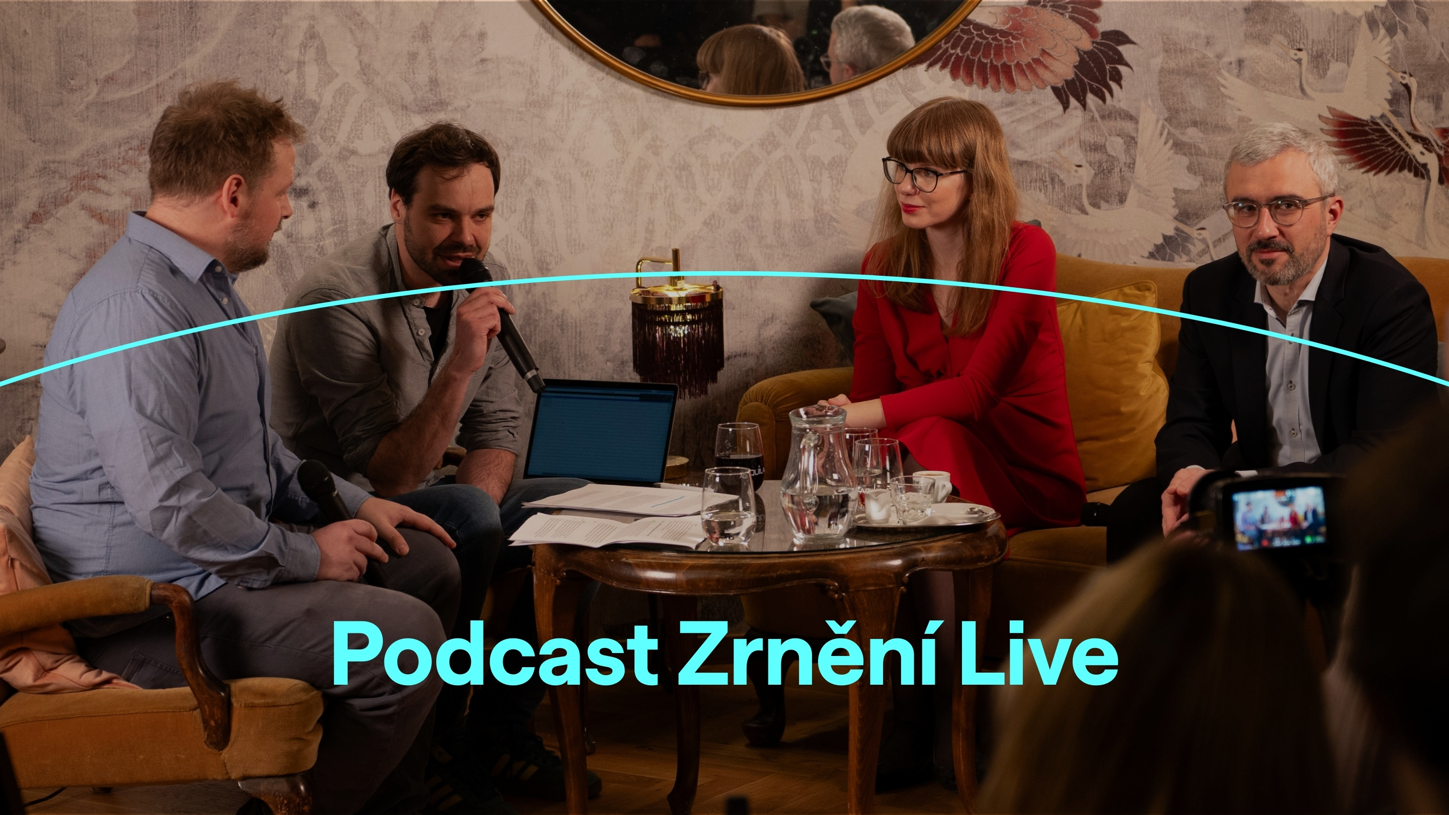 Grafika, na které je fotografie tří mužů a jedné ženy sedících na pohovce a v křesle, vedoucích spolu hovor. Dole je text: Podcast Zrnění Live.
