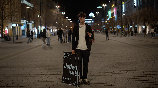 Muž stojí na ulici s plakátem Jednoho světa.