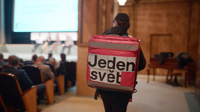 Muž kráčí po kinosálu s batohem kurýra, na kterém je nápis Jeden svět.