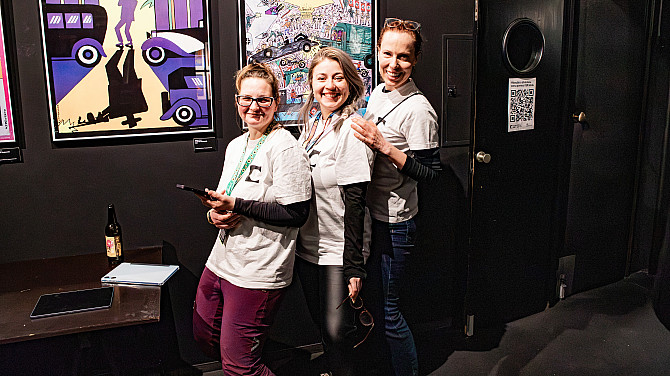 Tři mladé ženy stojí za sebou a se usmívají se. Na sobě mají trička s logem filmového festivalu Jeden svět a na krku pověšené cedulky Pořadatel.