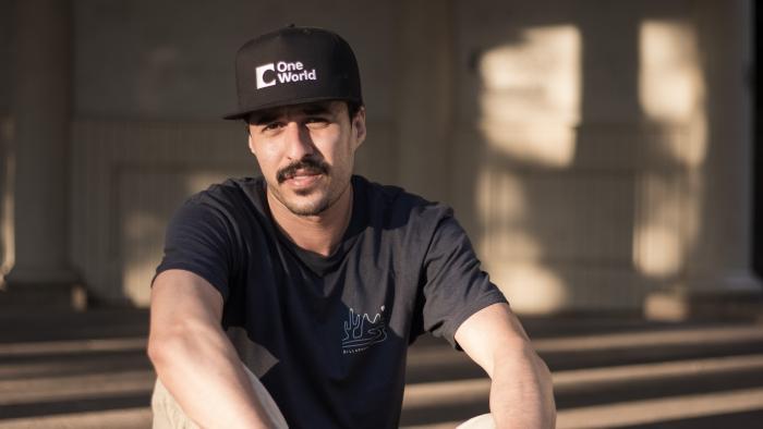 Muž s kšiltovkou sedí venku na zemi.