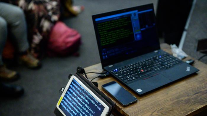 Simultánní přepis Na stole je položený notebook a vedle něj je umístěna obrazovka s přepisem.