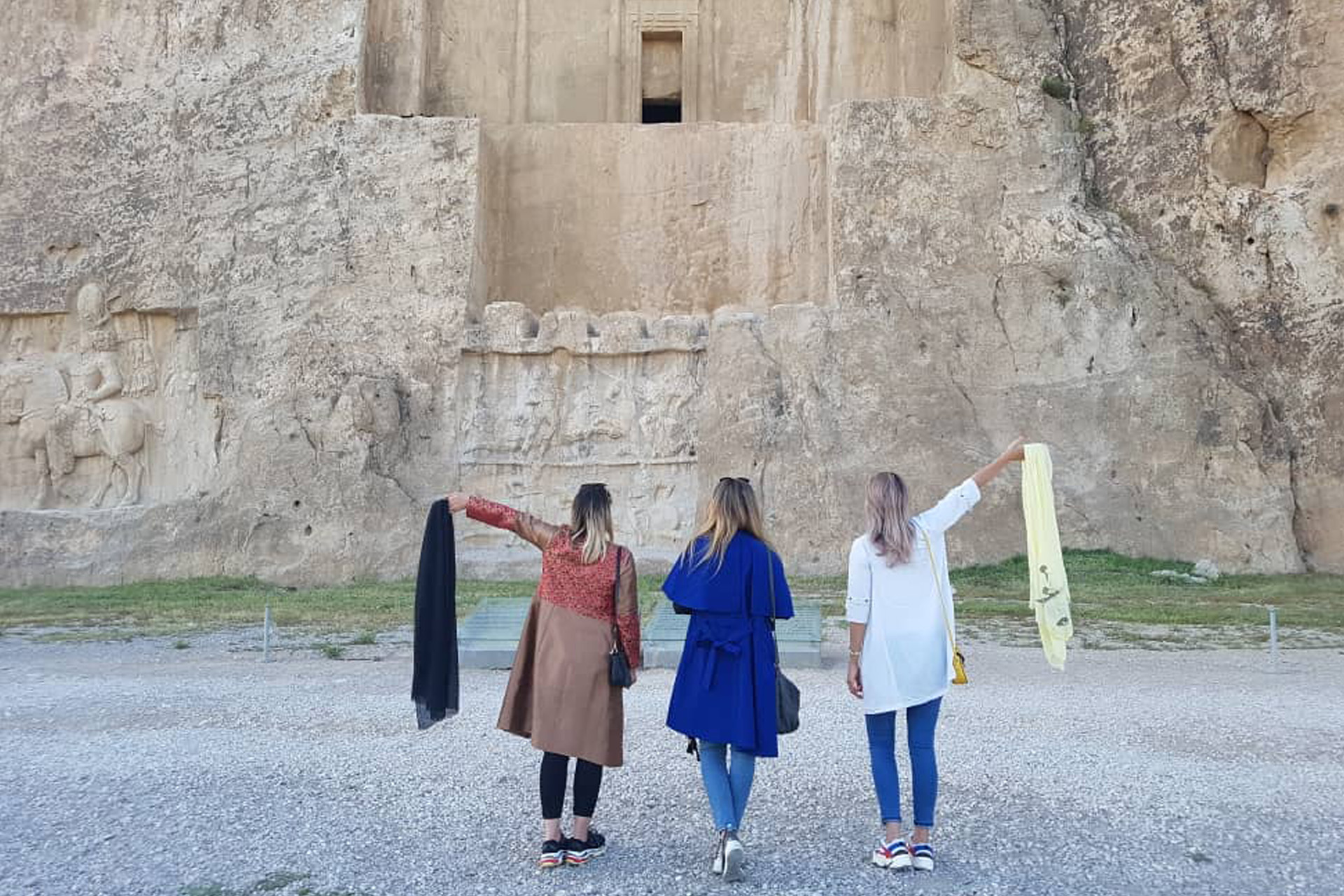 Tři západně oděné ženy stojí před skalním chrámem a odhazují muslimské šátky.