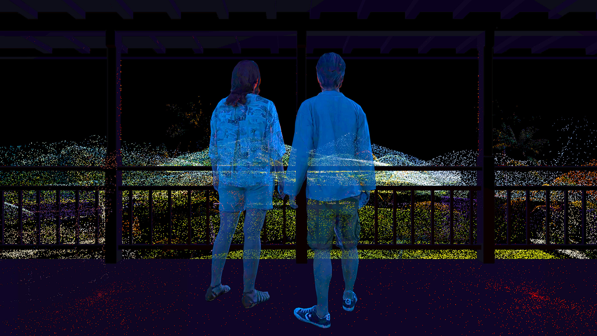 Zády k nám stojí na terase dvě osoby, které se drží za ruce. Koukají před sebe na rozpixelovanou krajinu. / Two people are standing on the terrace with their backs to us, holding hands. They are looking at the scattered landscape in front of them.