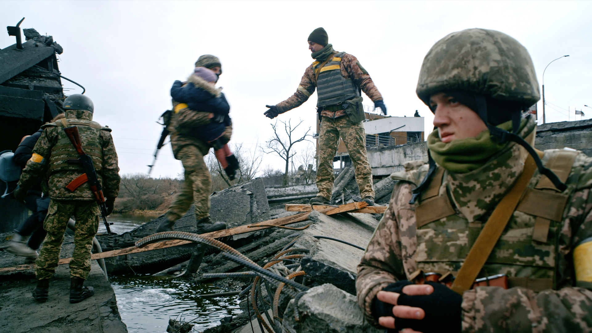 Ukrajinští vojáci stojí na troskách rozbombardovaného domu. Jeden z nich odnáší pryč malé dítě. / Ukrainian soldiers stand on the ruins of a bombed-out house. One of them is carrying away a small child.