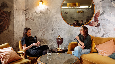 Dvě ženy sedí naproti sobe, jedna na pohovce a druhá v křesle a povídají si.