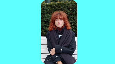 Žena v kabátě sedí na lavičce.