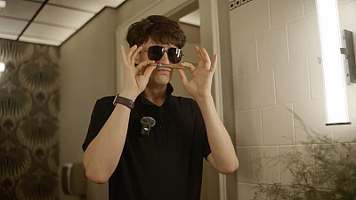 Muž v černých brýlích drží pod nosem doutník.