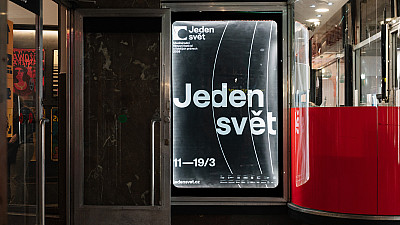 Plakát festivalu Jeden svět ve výloze v pasáži, na kterém je velký bílý nápis „Jeden svět“ a datum konání. Vedle výlohy je vstup do kina Světozor.