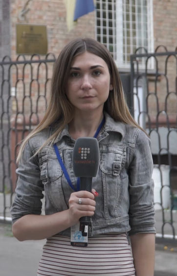 Mladá žena stojí venku před budovou a drží mikrofon.
