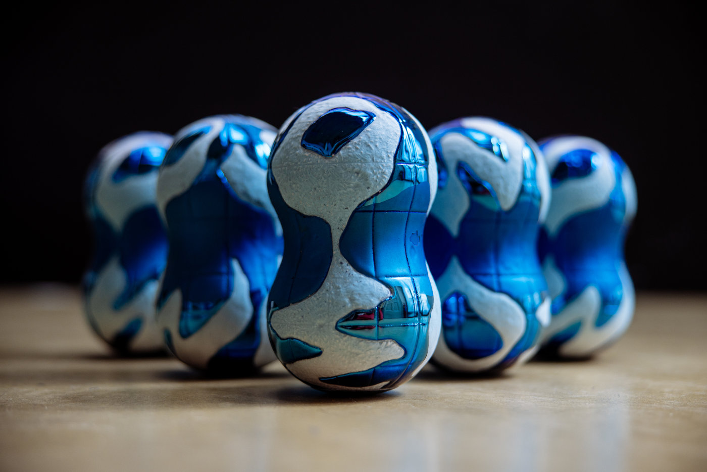 Pět modrých bowlingových kuželek s bílým vzorem stojí vedle sebe na podlaze.